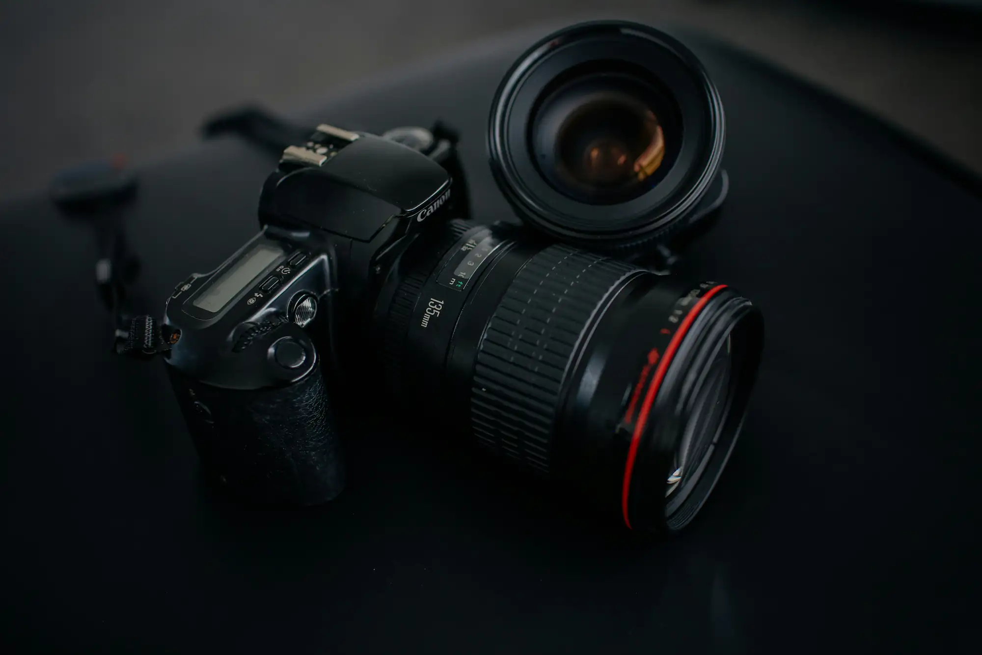 A black DSLR camera with a lens sits on a dark surface, ideal for photography enthusiasts and professionals.