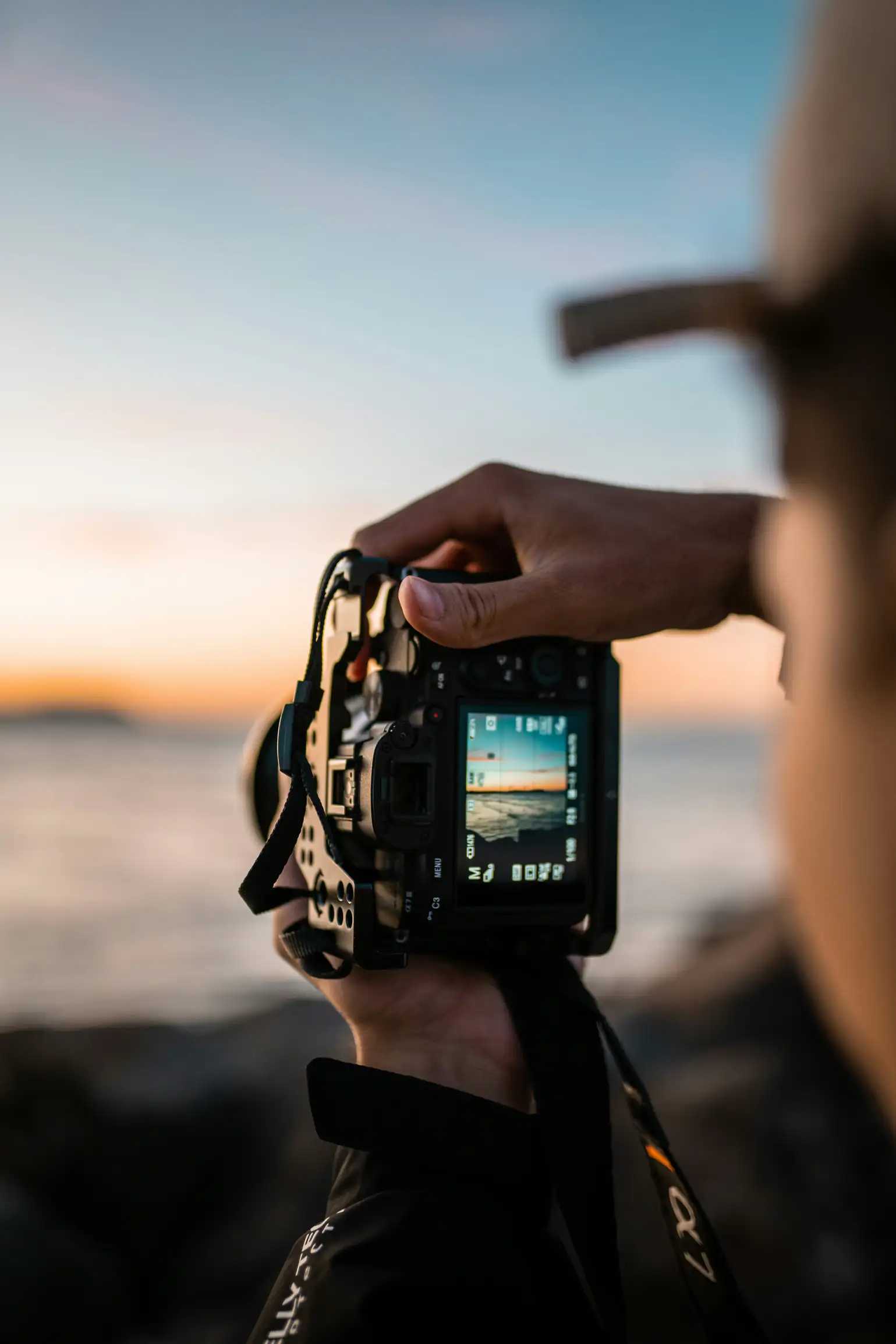 A person holds a digital camera, photographing an ocean sunset with the sunset image on the camera screen.