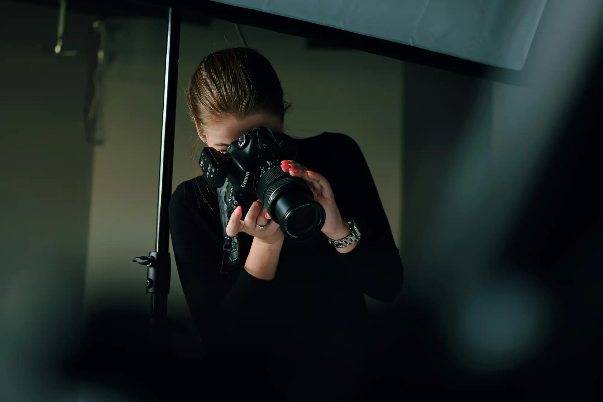 A person with tied-back hair holds a camera indoors, preparing to take a photograph for photography enthusiasts.